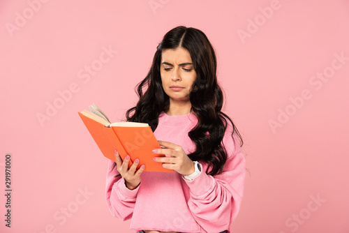 confused girl reading book, isolated on pink