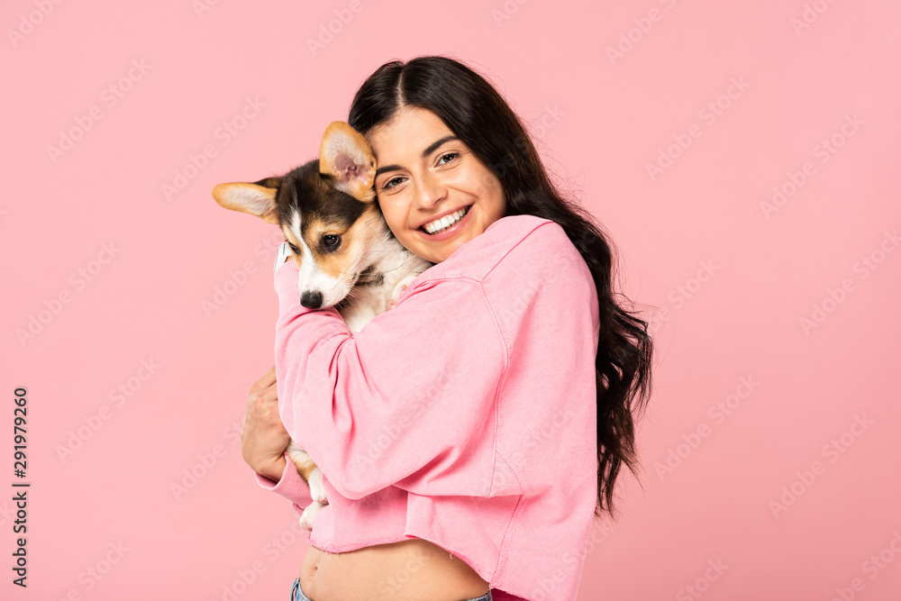 brunette young woman holding Welsh Corgi puppy, isolated on pink