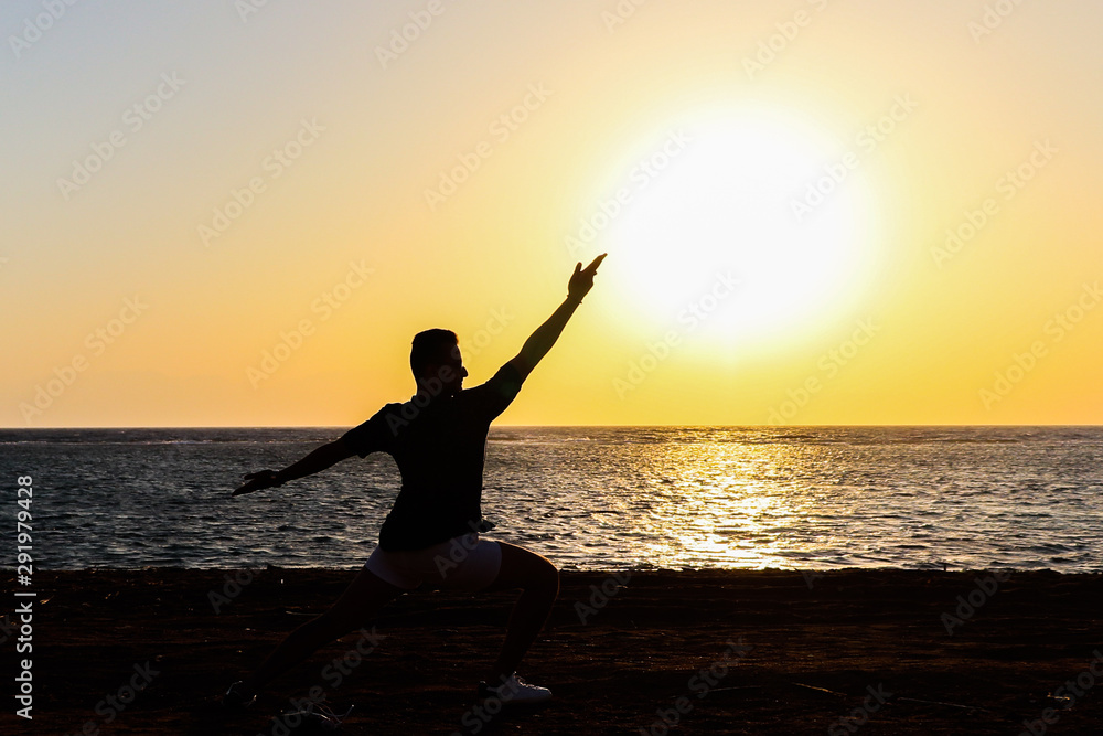 silhouette of a man doing yoga by the beach