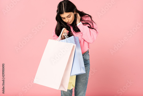 brunette woman looking into shopping bags, isolated on pink