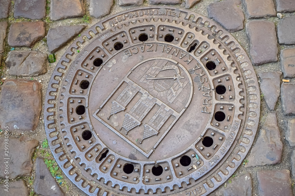 Metal sewer hatch with the coat of arms in the cobblestones title Prague Sewerage