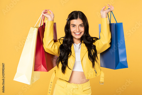 cheerful woman holding shopping bags, isolated on yellow