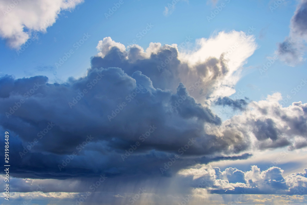 Powerful cumulonimbus dark cloud with heavy rain, tropical rain. Around the clear blue sky and the rising sun.