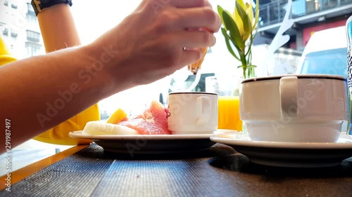 Woman in yellow shirt eating tasty breakfast with orange juice next to bright window in street cafe