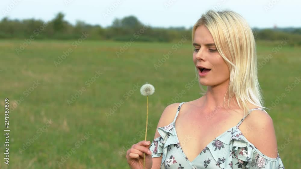 Beautiful young woman blows dandelion seeds in a field slow motion outdoors Beautiful young woman blows dandelion seeds in a field slow motion outdoors