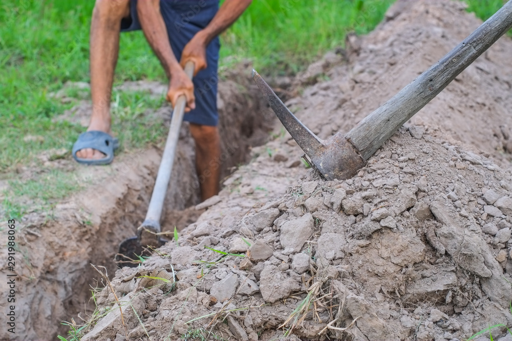Close-up pick axe with blurred man is using a hoe to dig the soil to build  a small canal. Stock Photo | Adobe Stock