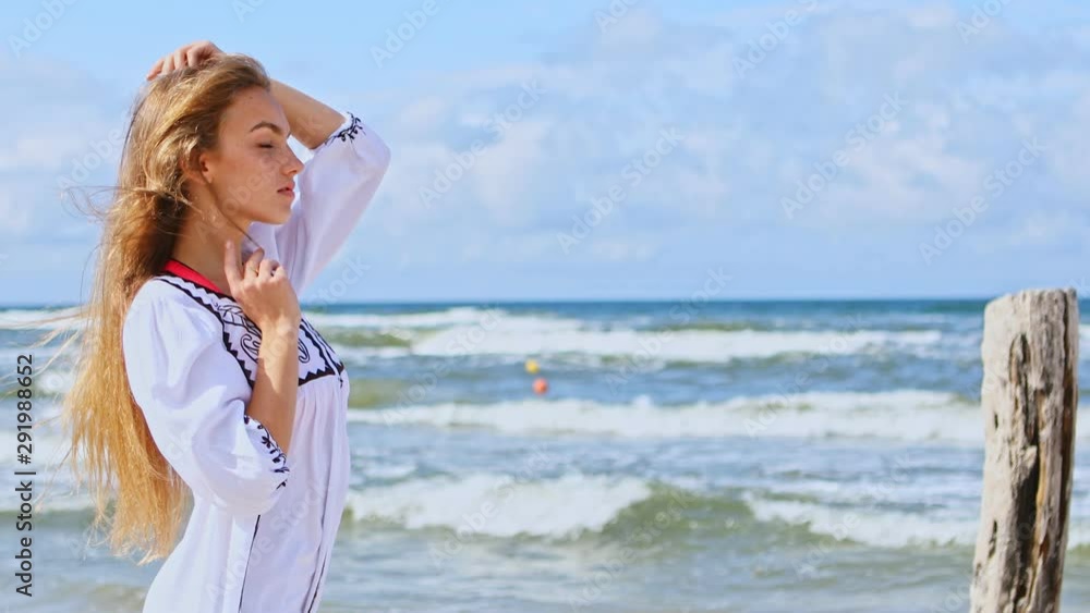 Close-up of a beautiful brunette young woman in a white dress which stands on the sandy beach in different pose. Close-up of a beautiful brunette young woman in a white dress which stands on the sandy beach in different pose.
