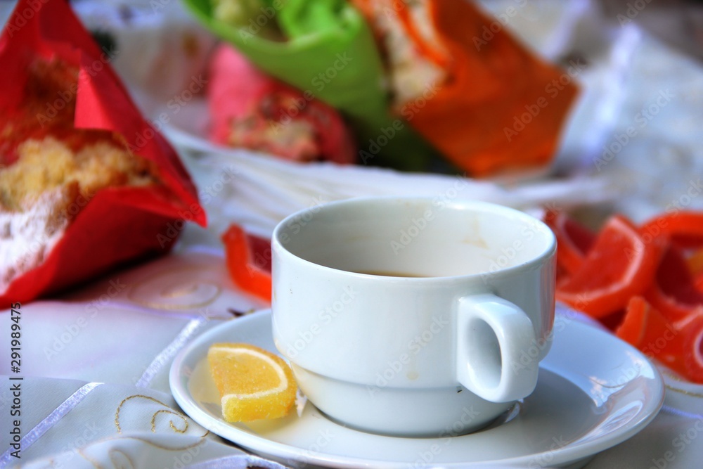 Cup of coffee, a bright yellow slice of marmalade on a saucer, a cupcake and sandwiches blurry. picnic in nature Cup of coffee, a bright yellow slice of marmalade on a saucer, a cupcake and sandwiches blurry. picnic in nature