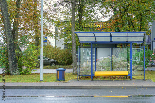 empty glass bus stop with yellow bench near road in city