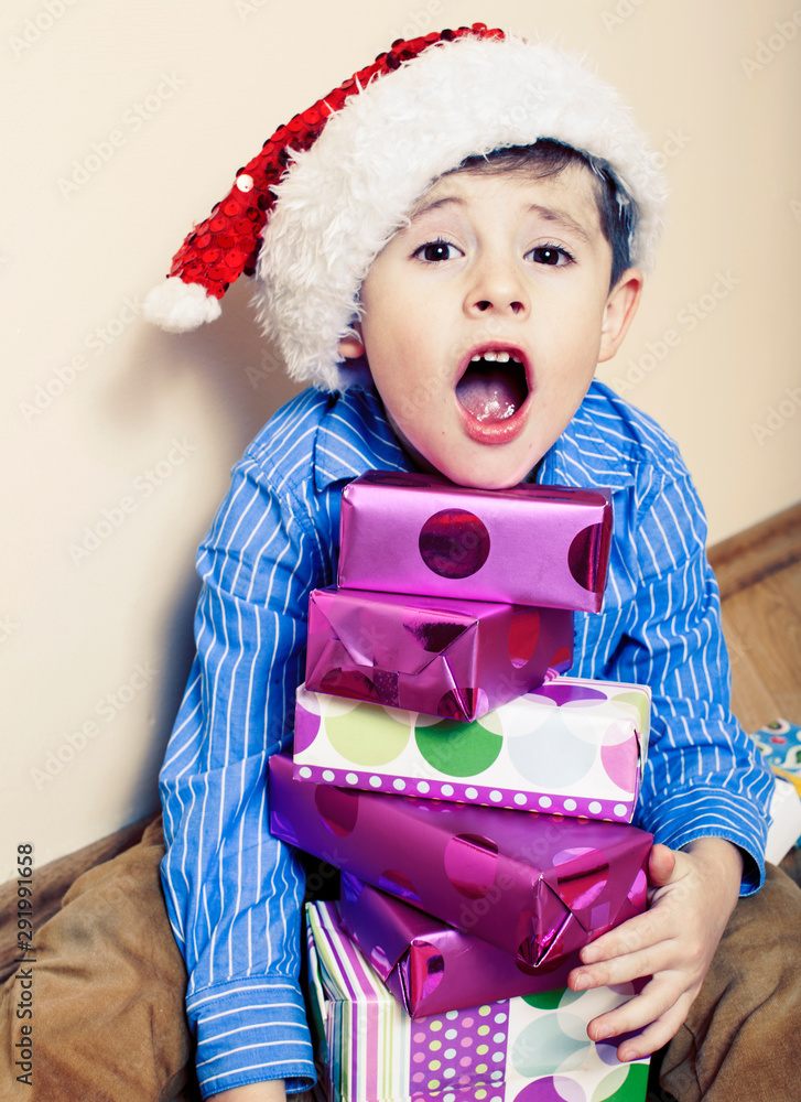 little cute boy with Christmas gifts at home. close up emotional face on boxes in santas red hat little cute boy with Christmas gifts at home. close up emotional face on boxes in santas red hat