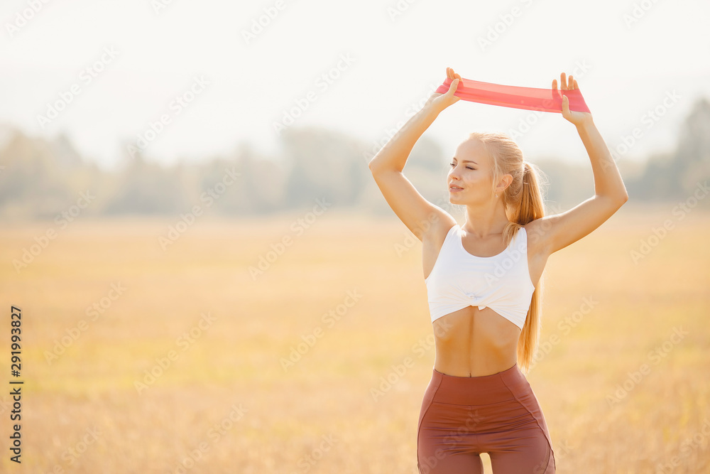 Beautiful girl athlete blonde performs exercises outdoors in park fitness stretching rubber bands Beautiful girl athlete blonde performs exercises outdoors in park fitness stretching rubber bands