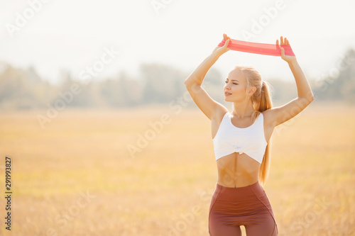 Beautiful girl athlete blonde performs exercises outdoors in park fitness stretching rubber bands