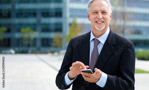 Mature businessman using his smartphone outdoor and smiling photo