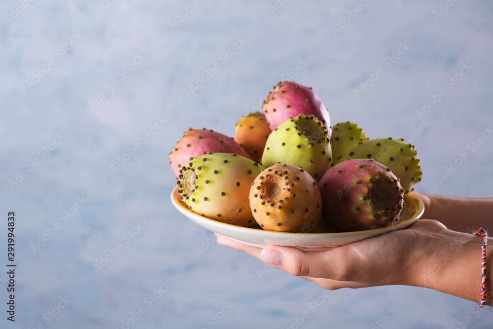 Female hands hold a plate with ripe fresh fruits of prickly pear on a gray background, selective focus