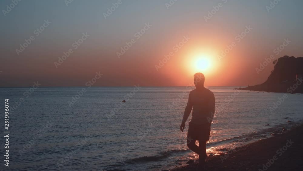 A young man walks along the shore against the backdrop of a sea sunset. A man walks along the beach on a sunset background. Silhouette of a man at sea sunset on the coast. A young man walks along the shore against the backdrop of a sea sunset. A man walks along the beach on a sunset background. Silhouette of a man at sea sunset on the coast.