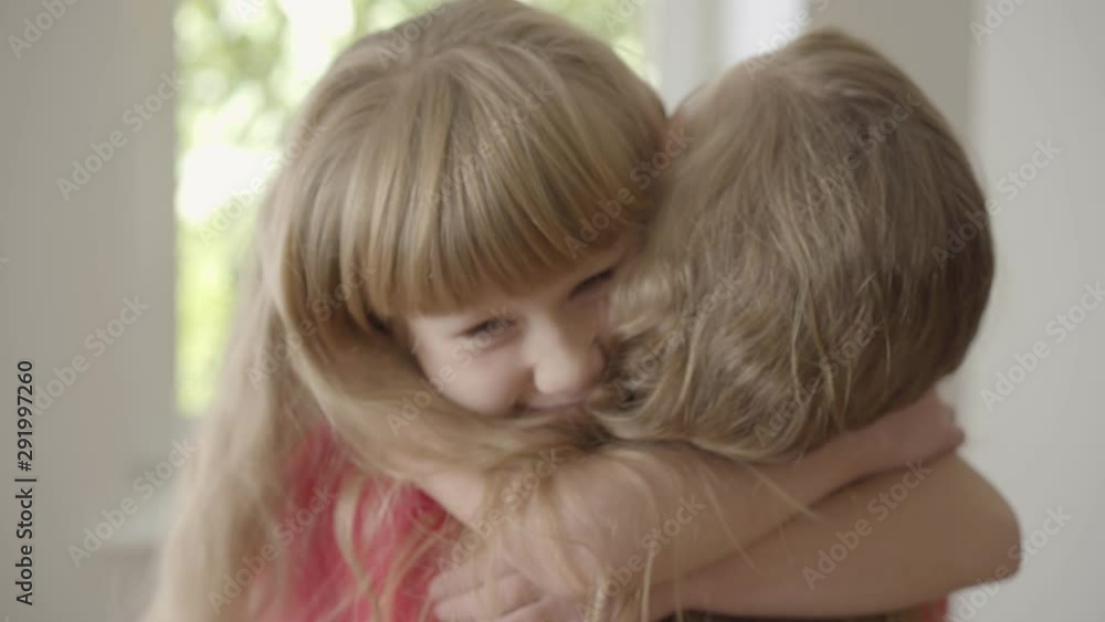 Cute little caucasian girl kissing caucasian woman on the cheek. Daughter hugging tight her mother with a long curly hair. Close-up. Cute little caucasian girl kissing caucasian woman on the cheek. Daughter hugging tight her mother with a long curly hair. Close-up.