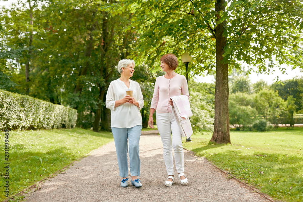 old age, retirement and people concept - two senior women or friends drinking coffee, walking and talking at park old age, retirement and people concept - two senior women or friends drinking coffee, walking and talking at park