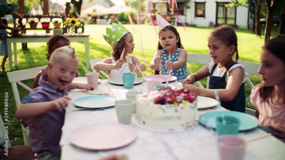 Down syndrome child with friends on birthday party outdoors in garden. Down syndrome child with friends on birthday party outdoors in garden.