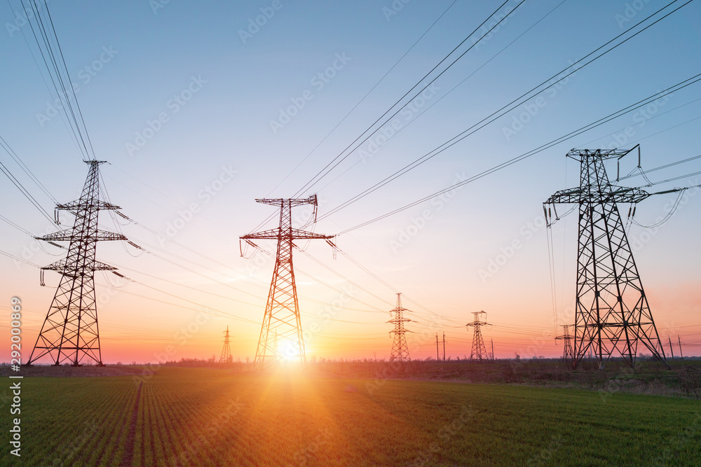High voltage lines and power poles and green agricultural landscape during sunrise.