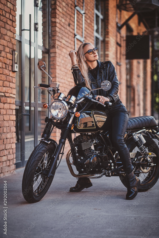 There are sexy mature woman in sunglasses and black leather clothing on the bike.