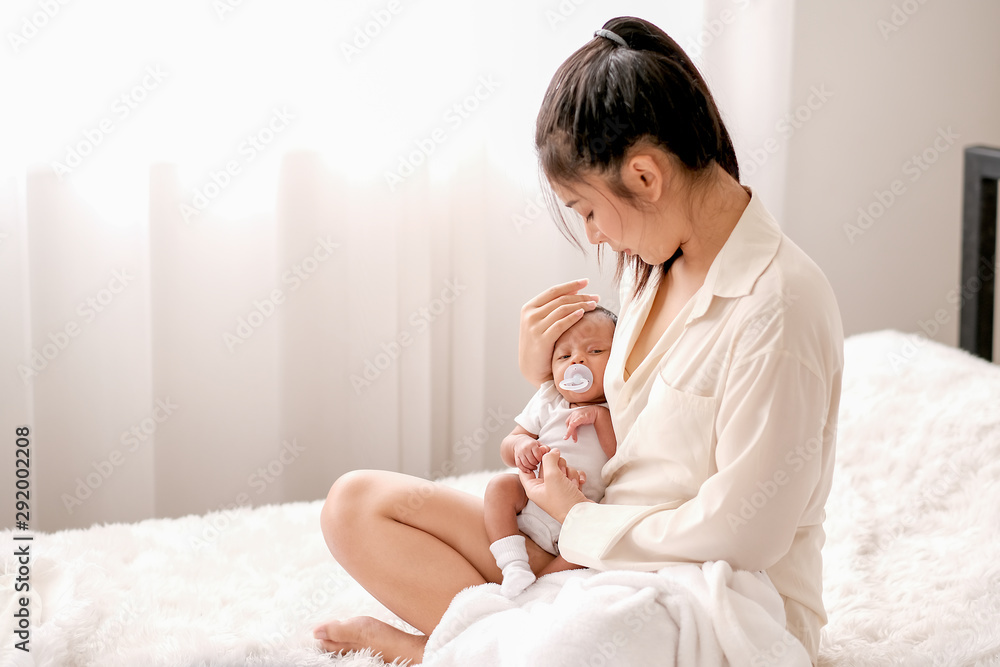 Soft blur image of beautiful Asian mother hold her newborn baby with baby teat on the white bed. Soft blur image of beautiful Asian mother hold her newborn baby with baby teat on the white bed.