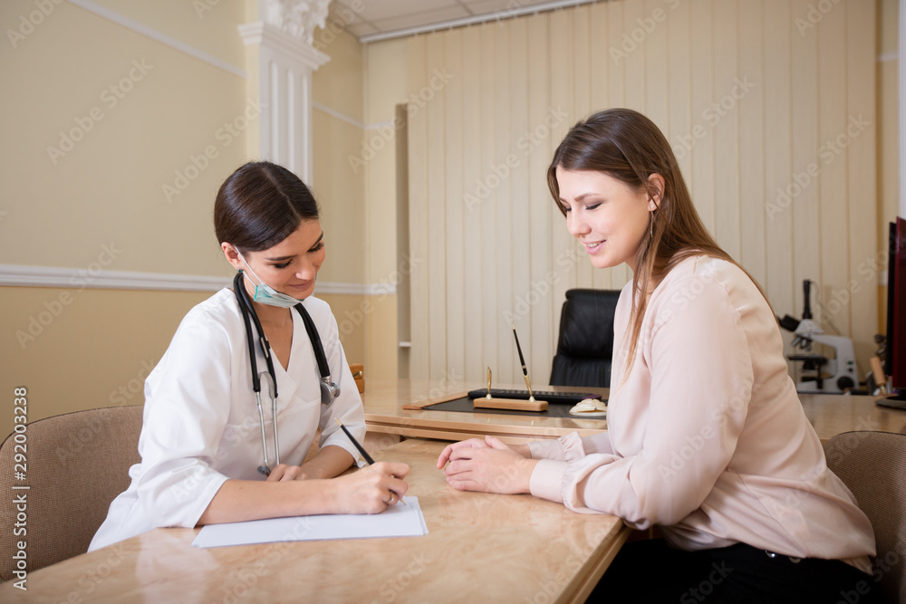Fototapeta premium Female doctor sitting at the desk in the office and writing a prescription to the patient.