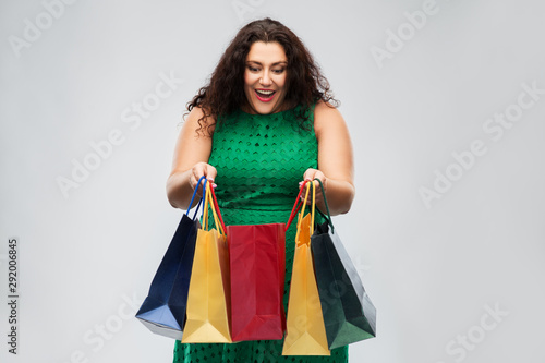 sale, outlet and consumerism concept - happy woman in green dress with shopping bags over grey background