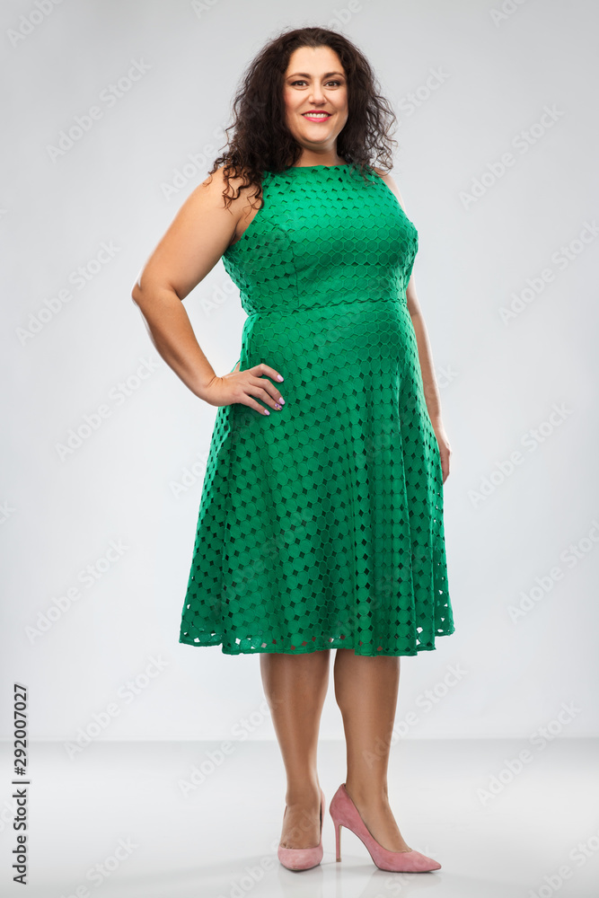 Naklejka premium people and portrait concept - happy woman in green dress posing over grey background