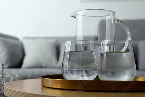 Tray with jug and glasses of water on table in room, space for text. Refreshing drink