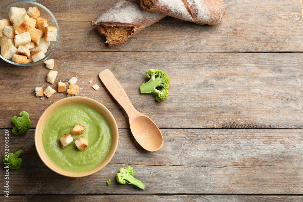 Flat lay composition with bowl of broccoli cream soup on wooden table, space for text