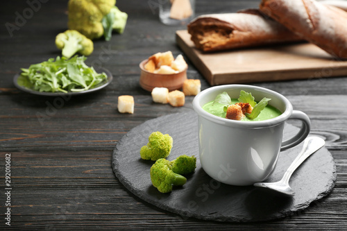 Cup of broccoli cream soup with croutons served on black wooden table, space for text