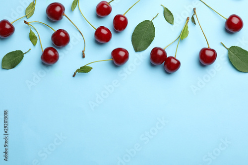 Leinwand Poster Tasty ripe cherries with leaves on light blue background, flat lay