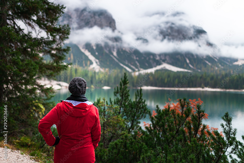 Women with red rain jacket enjoying the peaceful mystic view of a mountain lake with cloudy dramatic mountains in the background on a rainy autumn day. Women with red rain jacket enjoying the peaceful mystic view of a mountain lake with cloudy dramatic mountains in the background on a rainy autumn day.