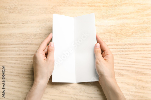 Young woman holding blank brochure at light wooden table, top view. Mock up for design