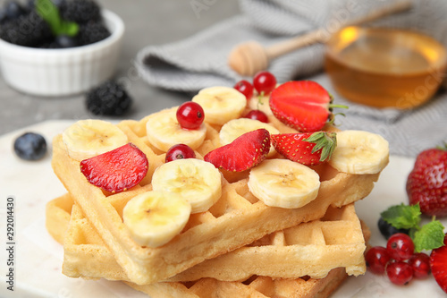 Board with delicious waffles and fresh berries on grey table, closeup