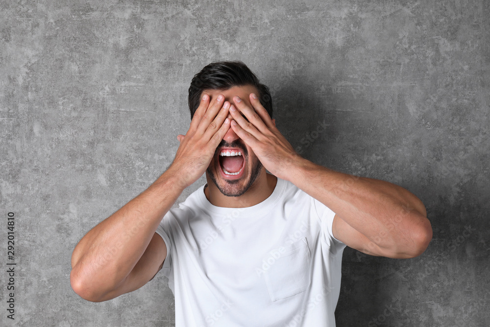 Young man being blinded and covering eyes with hands on grey background Young man being blinded and covering eyes with hands on grey background