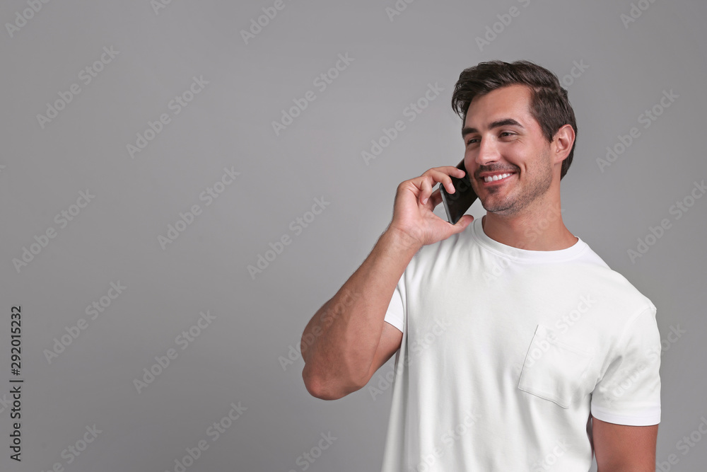 Handsome young man talking on smartphone against grey background. Space for text