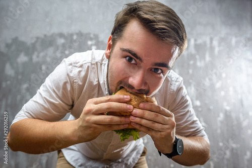 Portrait of a young man biting hamburger with mouth wide open