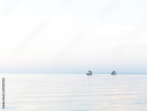 Two boats anchored off shore with an outgoing tide and clear sky at sunset.