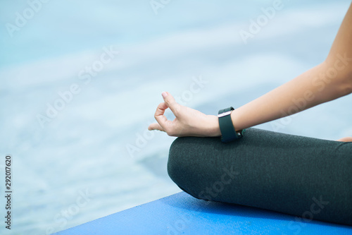 Close-up of young woman sitting in lotus position on exercise mat and meditating outdoors