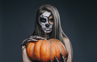 Attractive female with spooky makeup and pumpkin