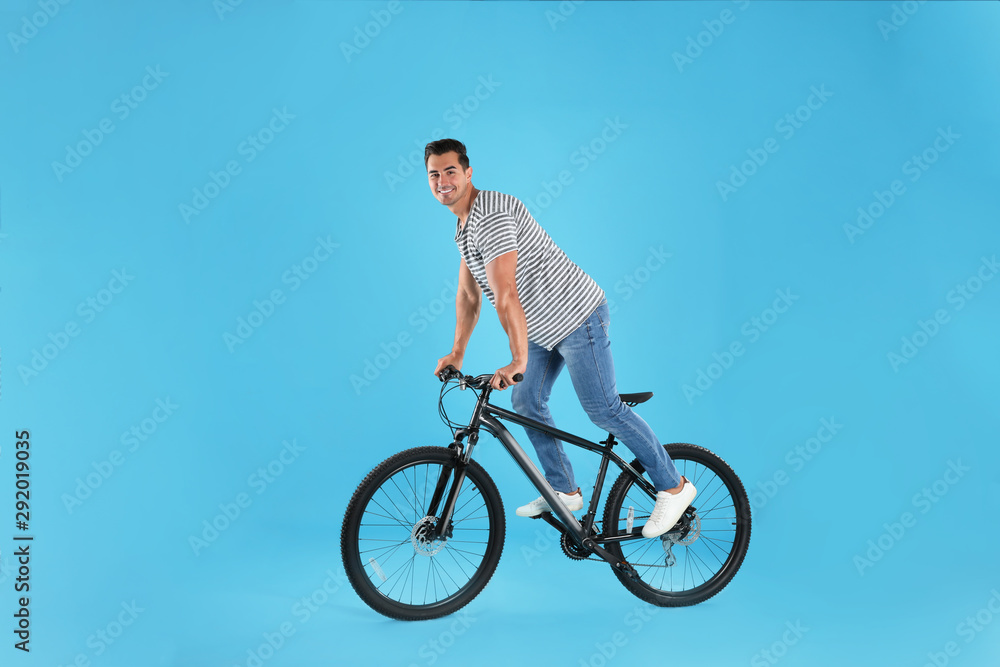 Handsome young man with modern bicycle on light blue background Handsome young man with modern bicycle on light blue background
