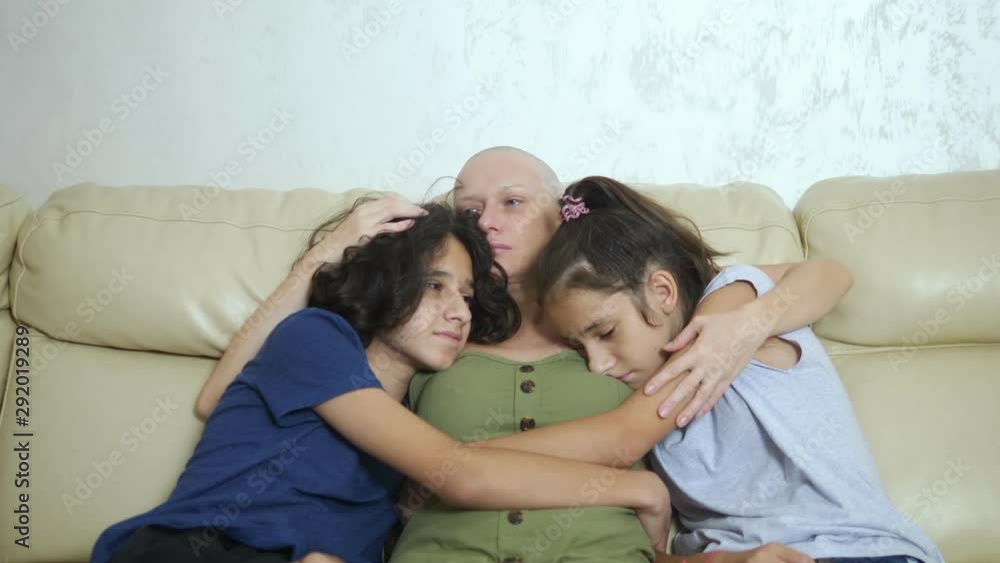 bald exhausted mother after cancer chemotherapy hugs her adolescent children sitting on a sofa bald exhausted mother after cancer chemotherapy hugs her adolescent children sitting on a sofa