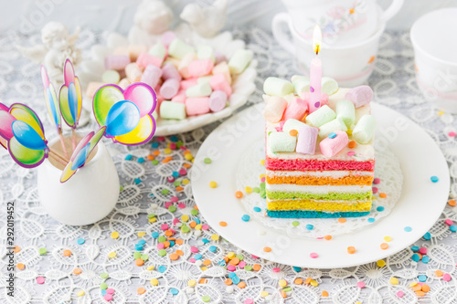 Rainbow birthday cake with marshmallows. Balls, confetti on the festive table.