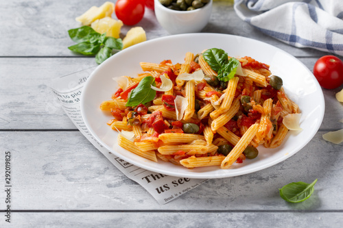 Traditional pasta putanesca with tomato sauce (capers, onions, garlic, anchovies). Tasty Italian food with Parmesan cheese, vegetarian Penne