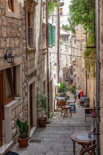 Beautiful narrow old stone street with stone houses and facades, flowers and  and chairs and tables in historic fortified Korcula town, Korcula Island, Dalmatia, Croatia  © Mislav