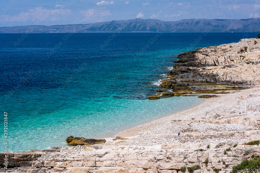 Beautiful stone beach on Proizd Island near Korcula Island, Dalmatia, Croatia, blue lagoon, pebbles, clear sea water and blue sky, Croatian islands in background, popular tourist destination  