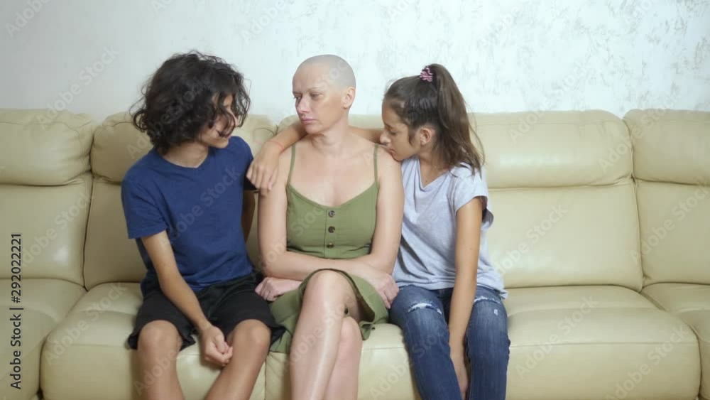 bald exhausted mother after cancer chemotherapy hugs her adolescent children sitting on a sofa bald exhausted mother after cancer chemotherapy hugs her adolescent children sitting on a sofa