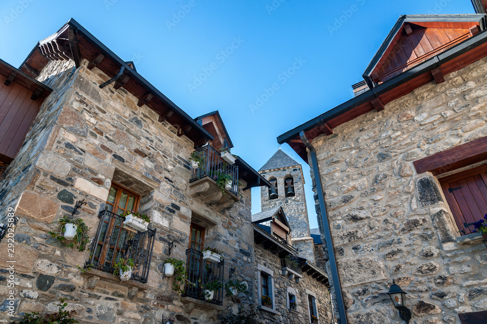 View of the bell tower of the village church of Lanuza with its picturesque stone houses, in the Pyrenees Mountains (Spain). View of the bell tower of the village church of Lanuza with its picturesque stone houses, in the Pyrenees Mountains (Spain).