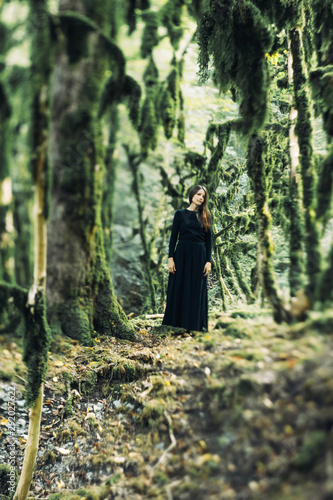Horror concept for halloween. A girl in a long black dress, like a ghost or a witch, in a mystical spooky forest.